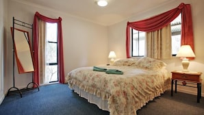 A bedroom with a bed, two bedside lamps, a nightstand, a mirror, and a window with curtains. - Serenity Grove (Fordwich)