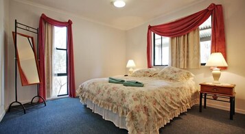 Un dormitorio con una cama, dos lámparas de noche, una mesita de noche, un espejo y un ventanal con cortinas.
