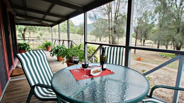 A covered outdoor seating area with a round glass table, striped chairs, and potted plants. - Serenity Grove (Fordwich)