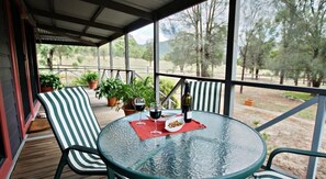 A covered outdoor seating area with a round glass table, striped chairs, and potted plants. - Serenity Grove (Fordwich)