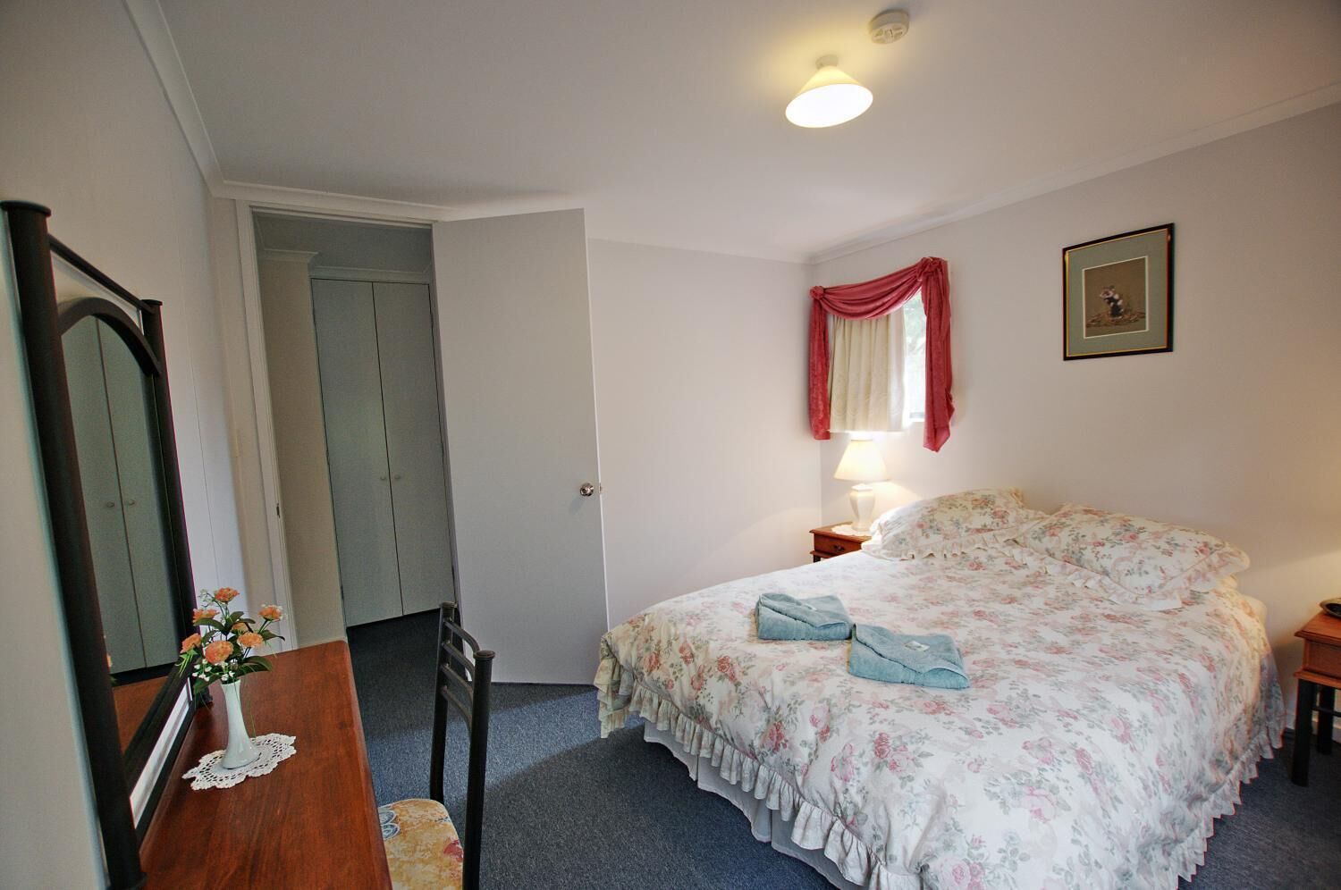 Une chambre à coucher comprenant un lit, une table de chevet, une lampe, un miroir et une porte donnant sur une autre pièce.