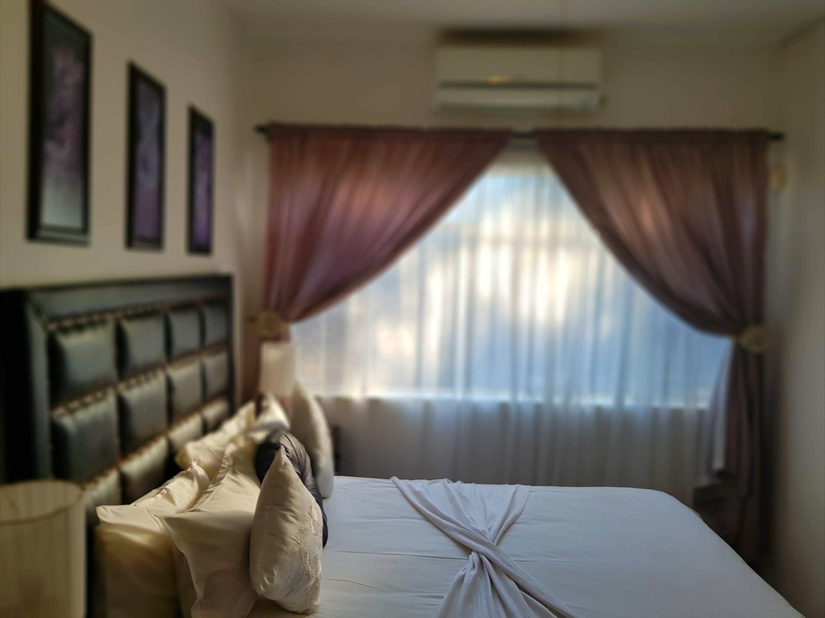 A hotel room with a neatly made bed, a headboard, and a window with curtains.