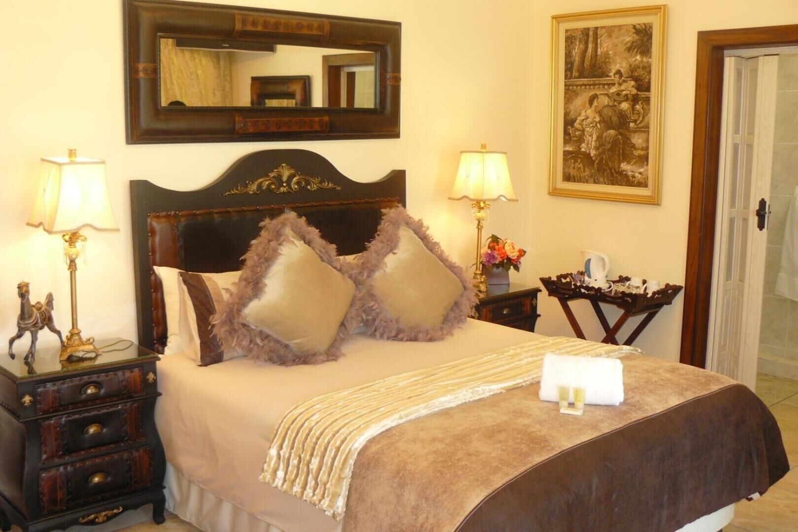 A neatly made bed with a headboard, two bedside tables with lamps, a mirror, and a painting on the wall.