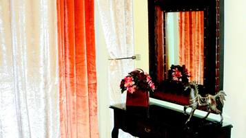 A room with a TV mounted on the wall, a wooden dresser with a mirror, a vase with flowers, and a chair.