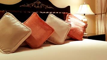 A bed with four pillows in shades of beige and orange, a dark wooden headboard, and a bedside table with a lamp.