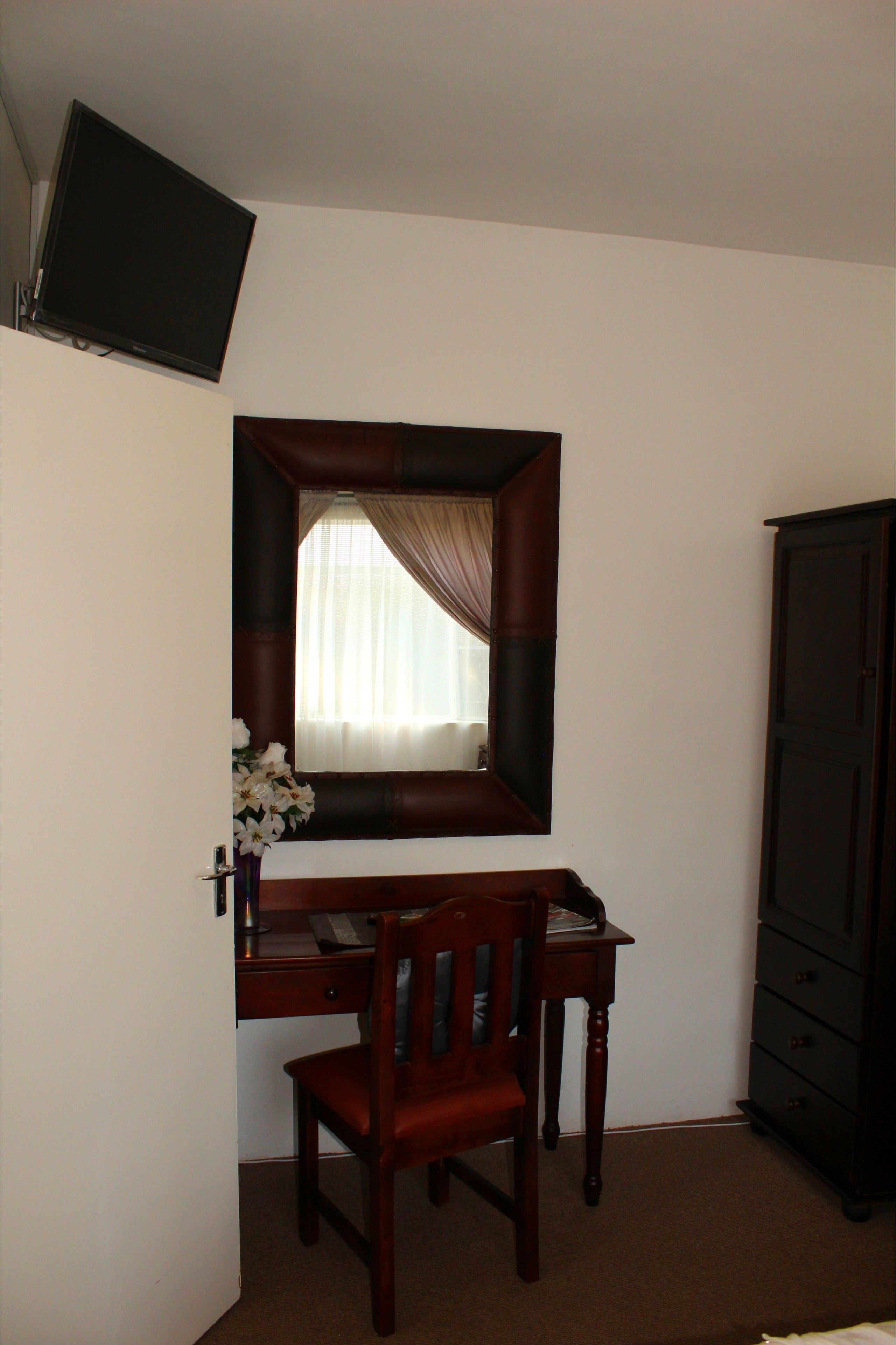 A room with a desk, chair, mirror, TV, and wardrobe.