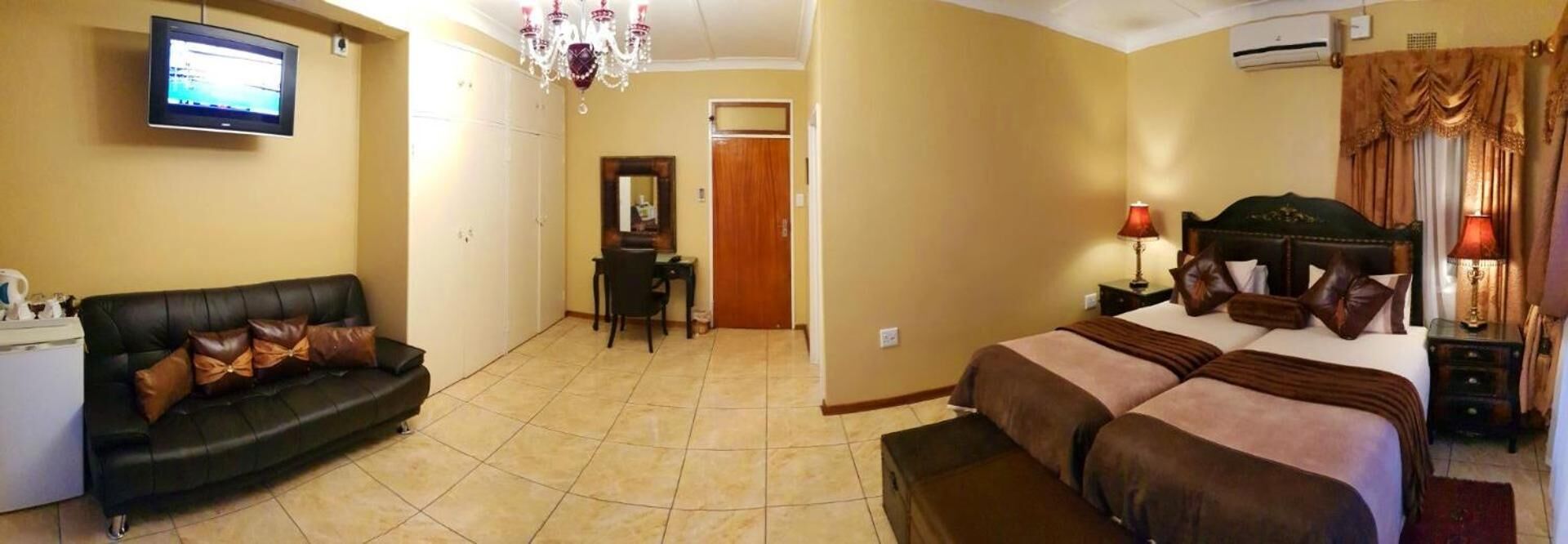Habitación de hotel con cama, sofá, televisor, candelabro y puerta.