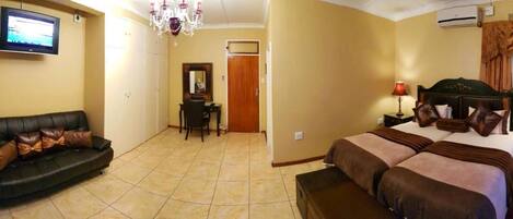 Habitación de hotel con cama, sofá, televisor, candelabro y puerta.