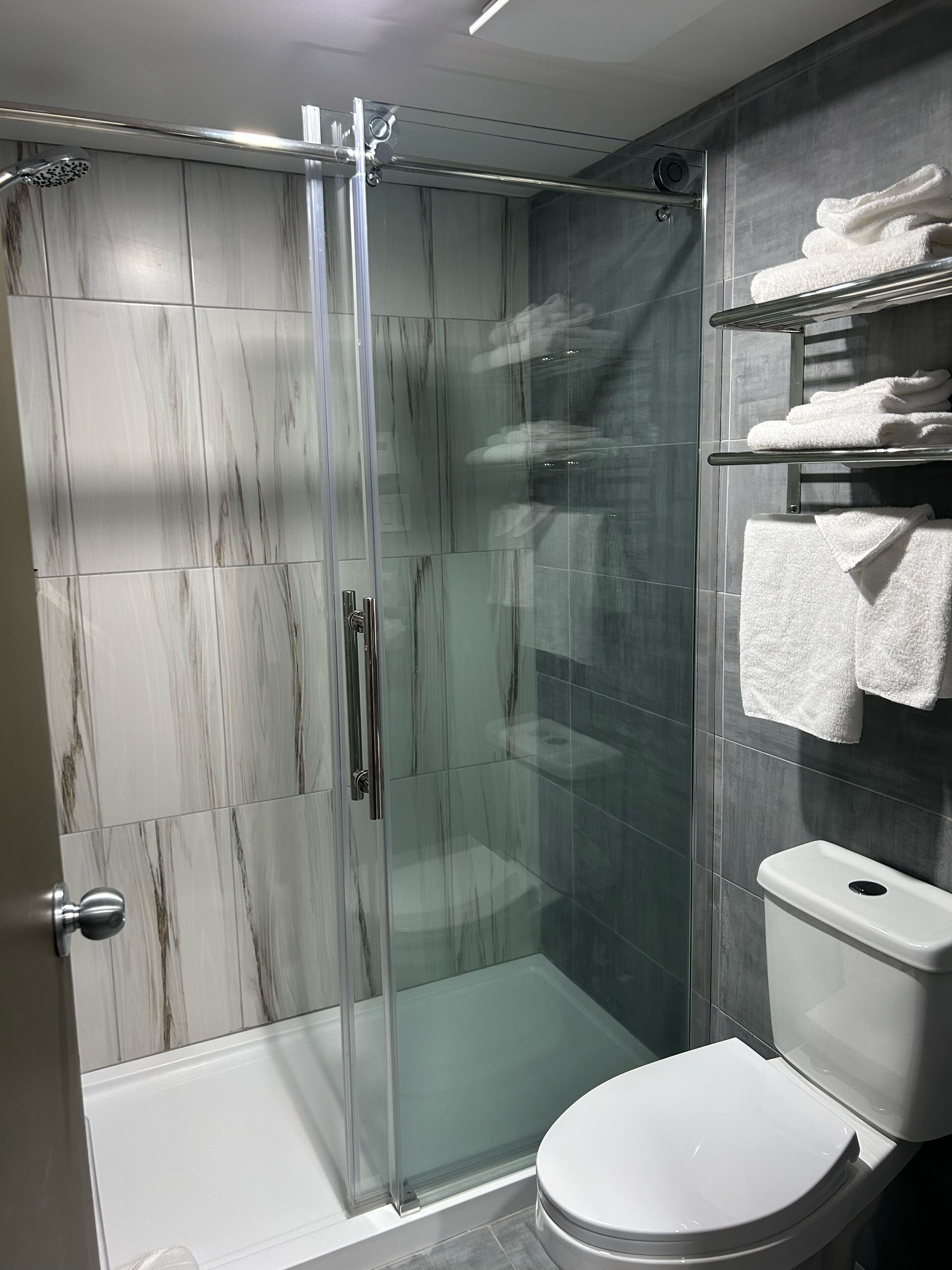 Un baño moderno con cabina de ducha de vidrio, inodoro y estante con toallas dobladas.