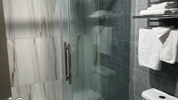 Un baño moderno con cabina de ducha de vidrio, inodoro y estante con toallas dobladas.