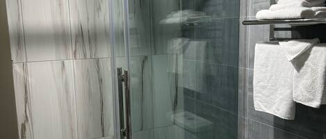 Un baño moderno con cabina de ducha de vidrio, inodoro y estante con toallas dobladas.
