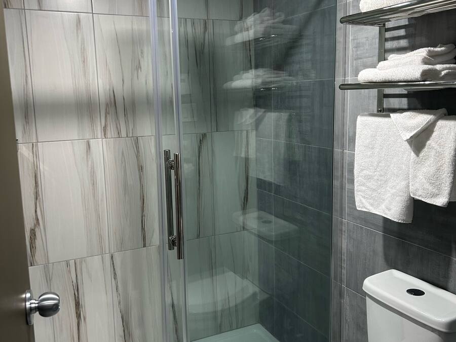 Un baño moderno con cabina de ducha de vidrio, inodoro y estante con toallas dobladas.
