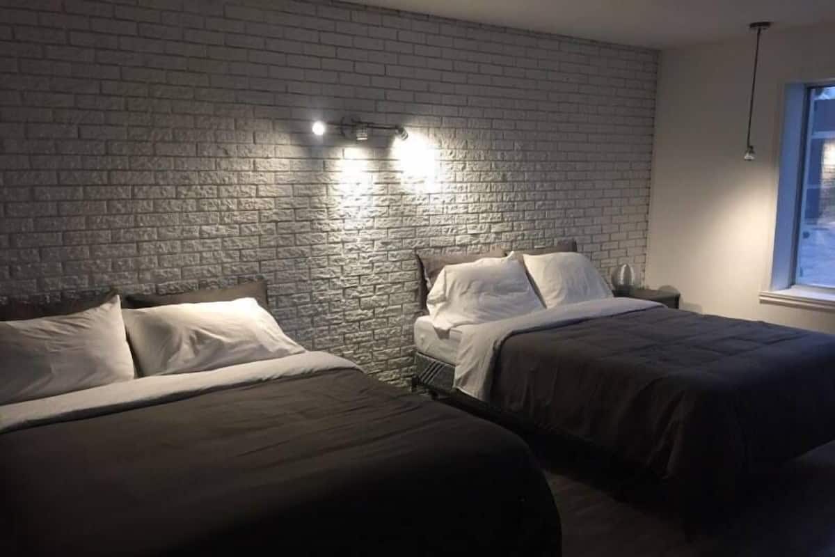 Una habitación con dos camas, una pared de ladrillo y una ventana.