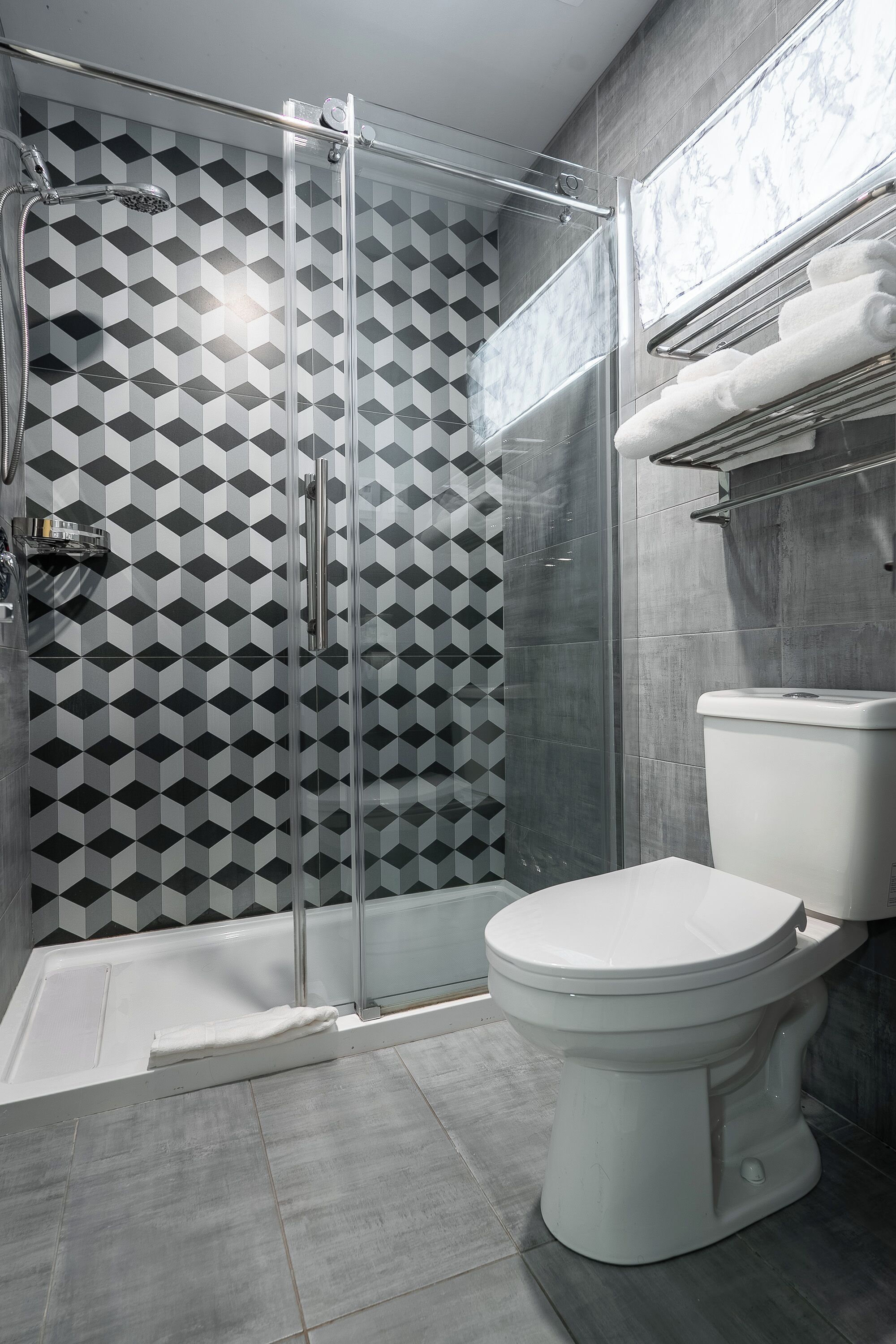 Un baño moderno con cabina de ducha de vidrio, inodoro blanco y pared con diseño.