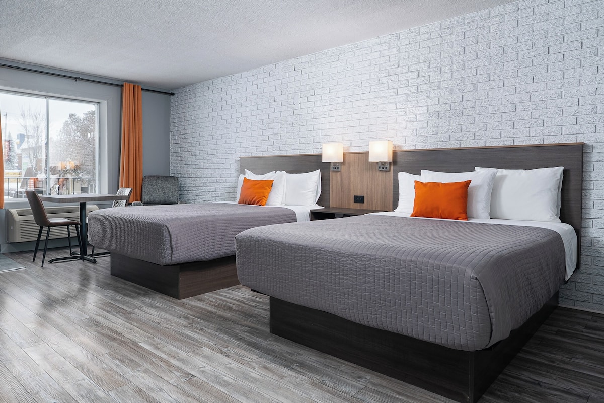 Habitación de hotel con dos camas, un escritorio y una ventana con cortinas.