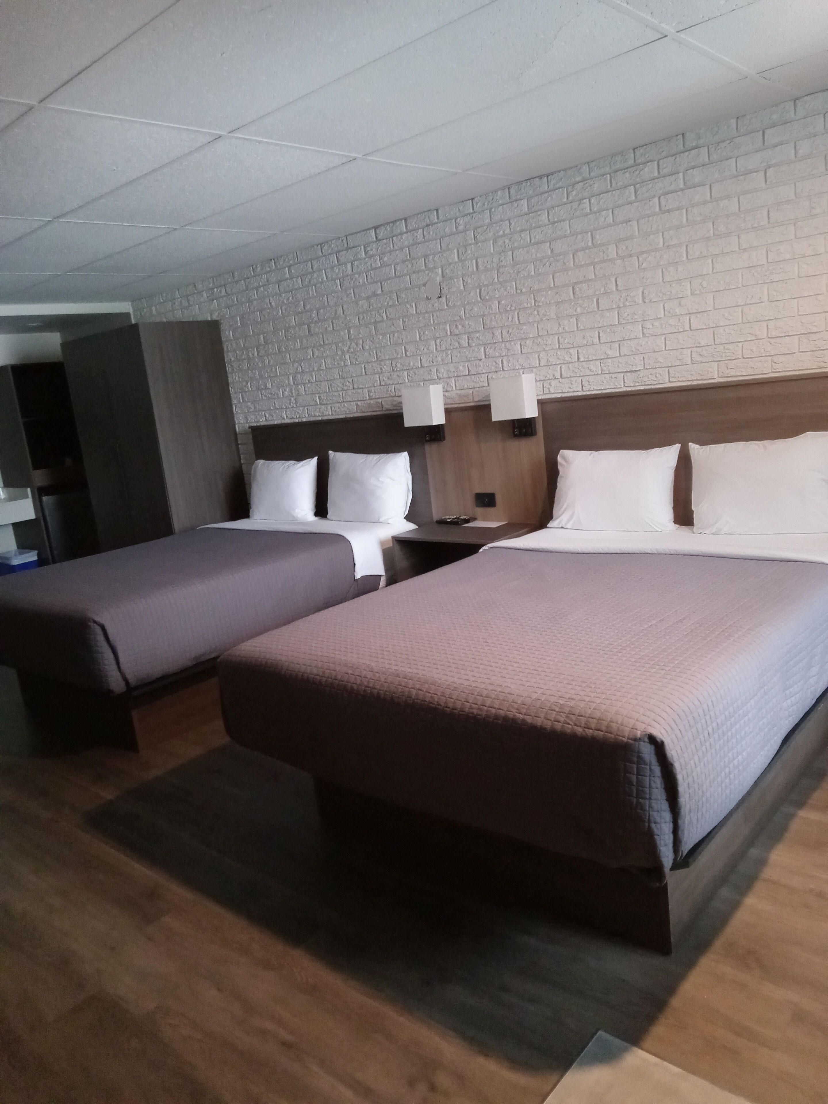 Ett hotellrum med två sängar, en vägg med tegelstensmönster och en sänggavel i trä.