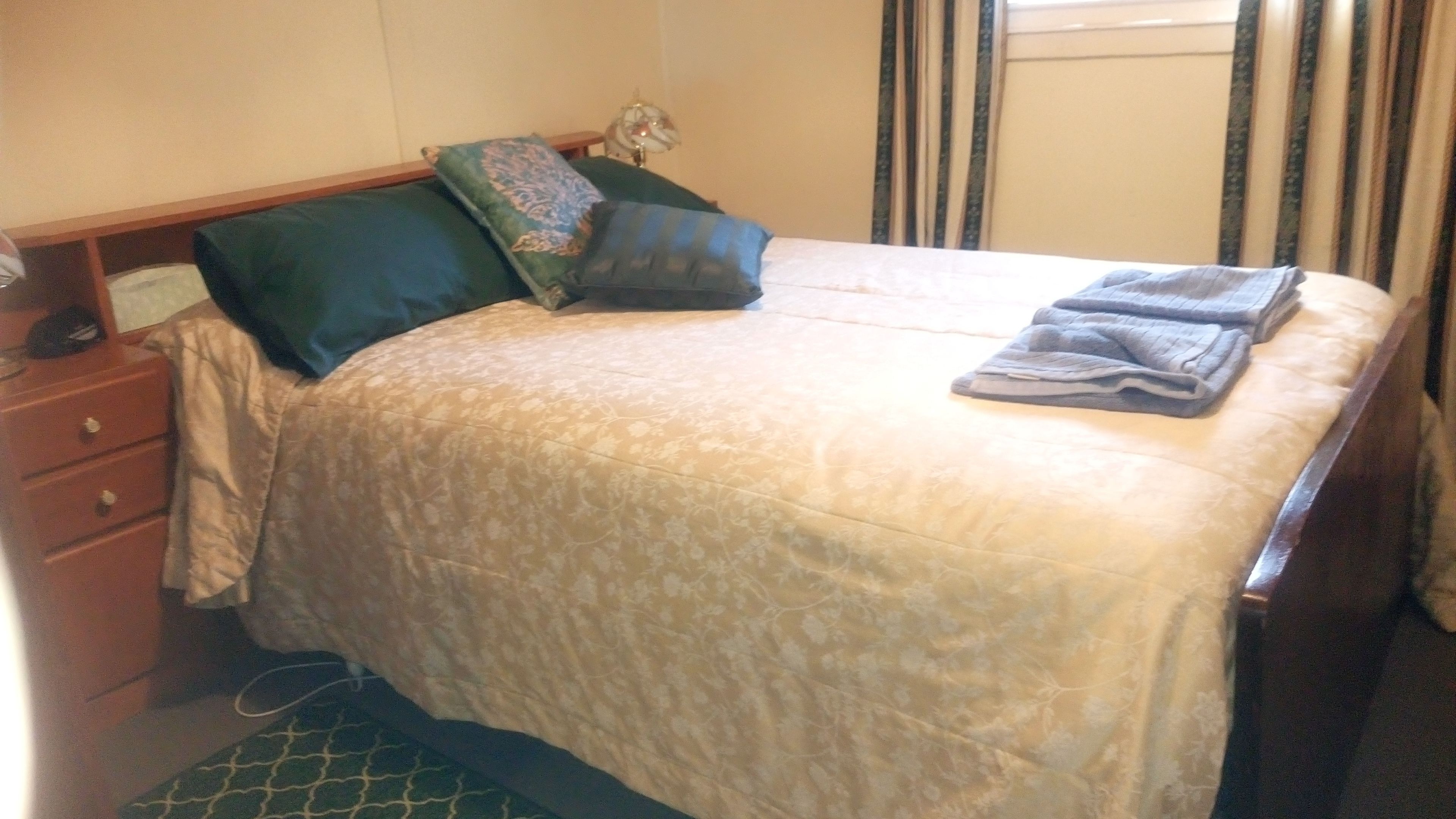 Un lit bien fait, recouvert d’une couvre-lit à motifs floraux, avec deux oreillers et une serviette pliée posée sur le côté droit.