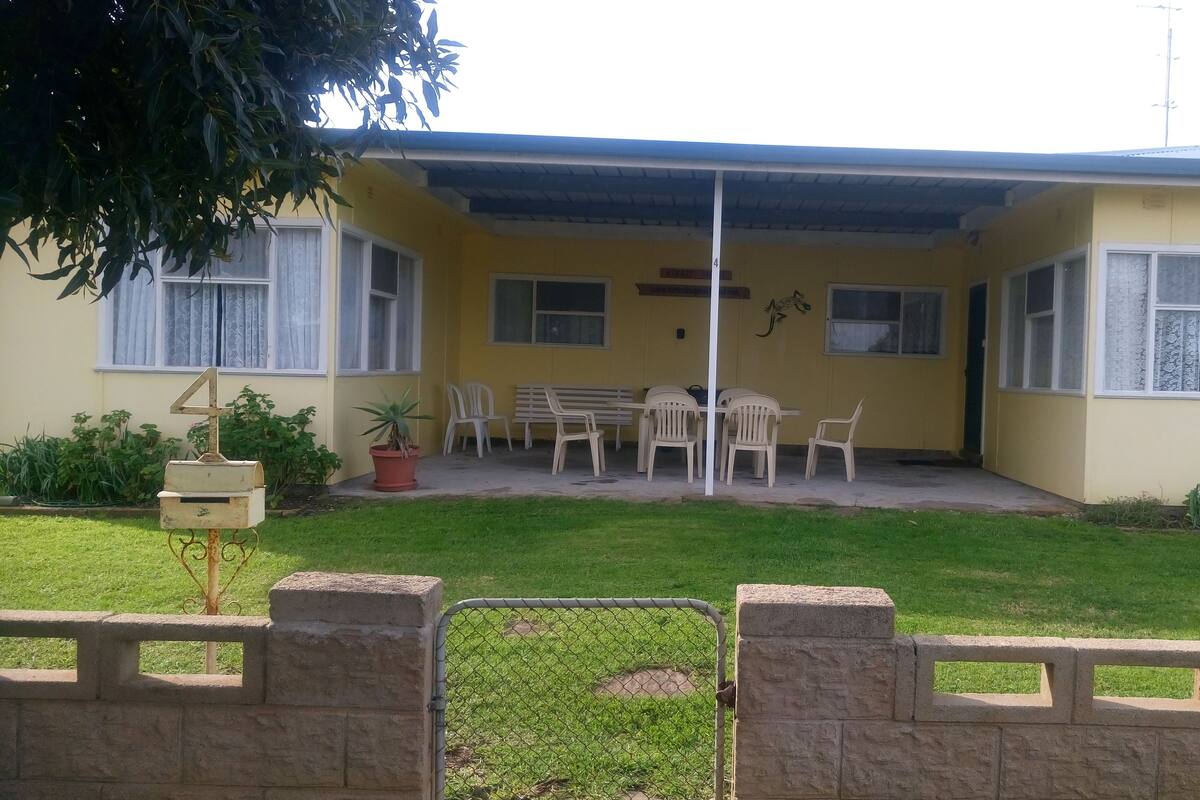 Un edificio amarillo con un porche cubierto, un buzón y una reja.