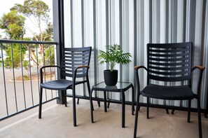 A balcony with two black chairs and a small table, a potted plant, and a view of trees and a parking lot. - Mansfield Apartments (Mansfield)