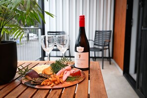 A wooden table with a charcuterie board, two wine glasses, and a bottle of wine on a balcony with chairs and a potted plant. - Mansfield Apartments (Mansfield)