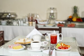 Una mesa de desayuno con tostadas, jamón, queso, café, una bandeja de fruta y jugo rojo.
