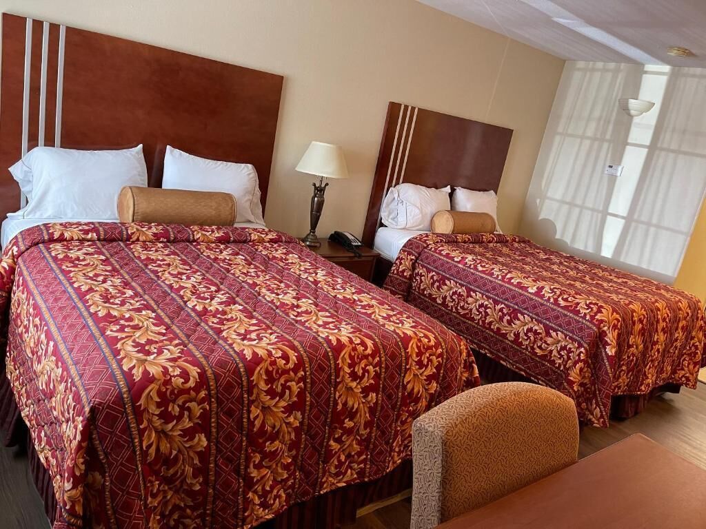 A hotel room with two beds, each with a patterned bedspread, a nightstand with a lamp, and a chair.