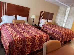 Une chambre d’hôtel avec deux lits, chacun recouvert d’une couvre-lit à motifs, une table de chevet avec une lampe et une chaise.