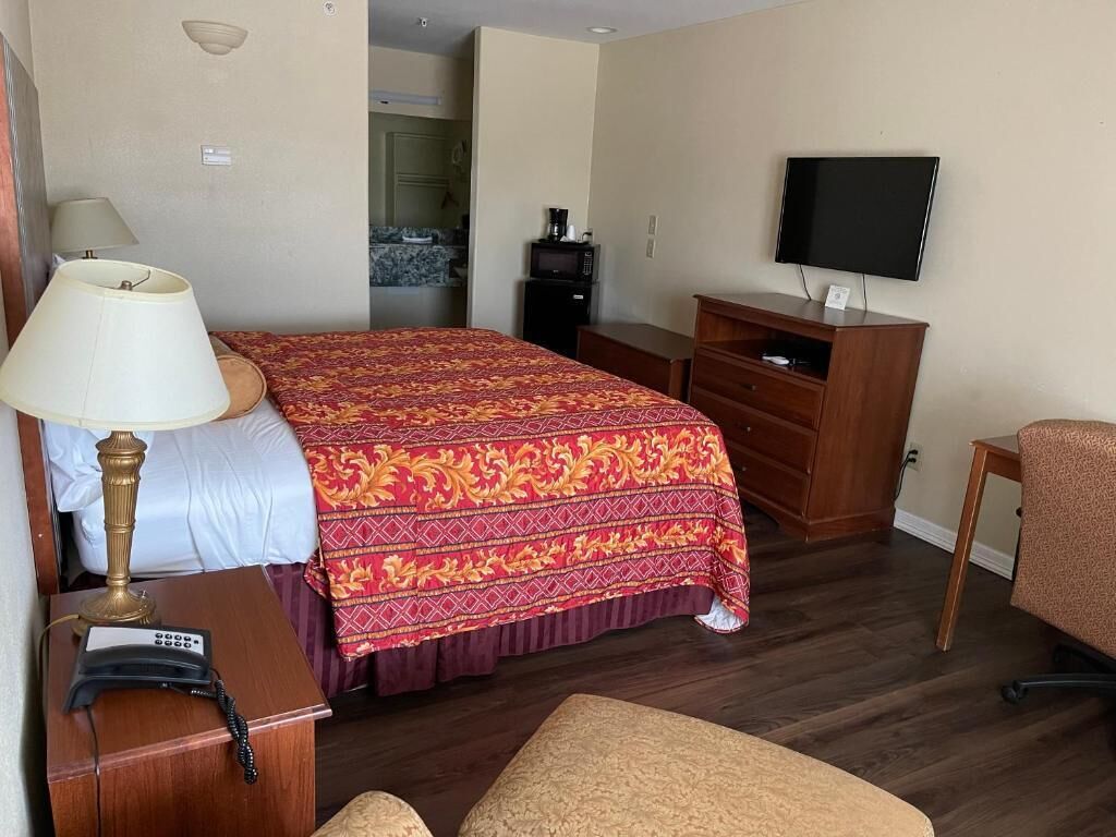 A hotel room with a bed, a desk with a lamp, a television, and a small kitchenette.