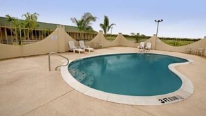 A swimming pool with a wavy edge, surrounded by a beige deck and white lounge chairs. - Riviera Inn & Suites (Riviera)