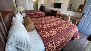A hotel room with two beds, a desk, a TV, and a mirror. - Riviera Inn & Suites (Riviera)