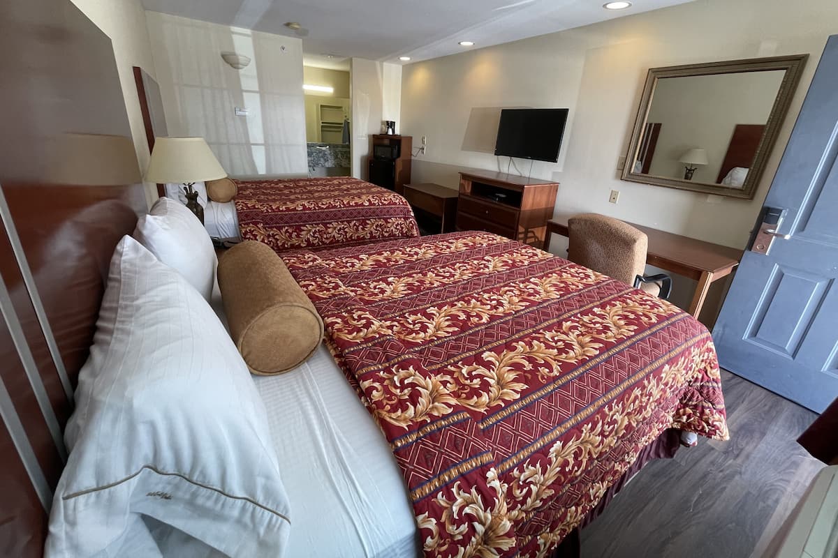 A hotel room with two beds, a desk, a TV, and a mirror.