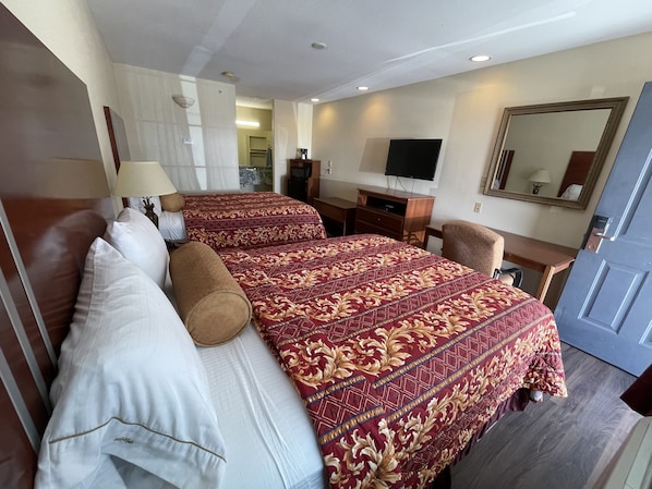 A hotel room with two beds, a desk, a TV, and a mirror.