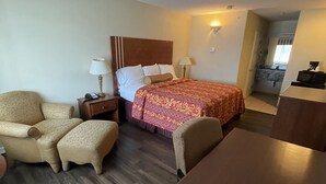 A hotel room with a bed, a chair, a table, a nightstand, and a lamp. - Riviera Inn & Suites (Riviera)