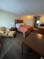 Quarto de hotel com cama, cadeira, mesa, mesa de cabeceira e luminária.
