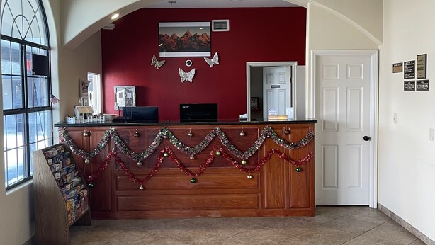 A reception area with a wooden desk, a chandelier, a large window, and a decorative tile floor. - Riviera Inn & Suites (Riviera)