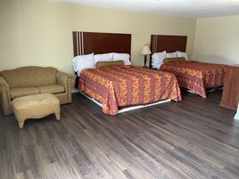 Quarto de hotel com duas camas, um sofá e uma mesa de cabeceira.