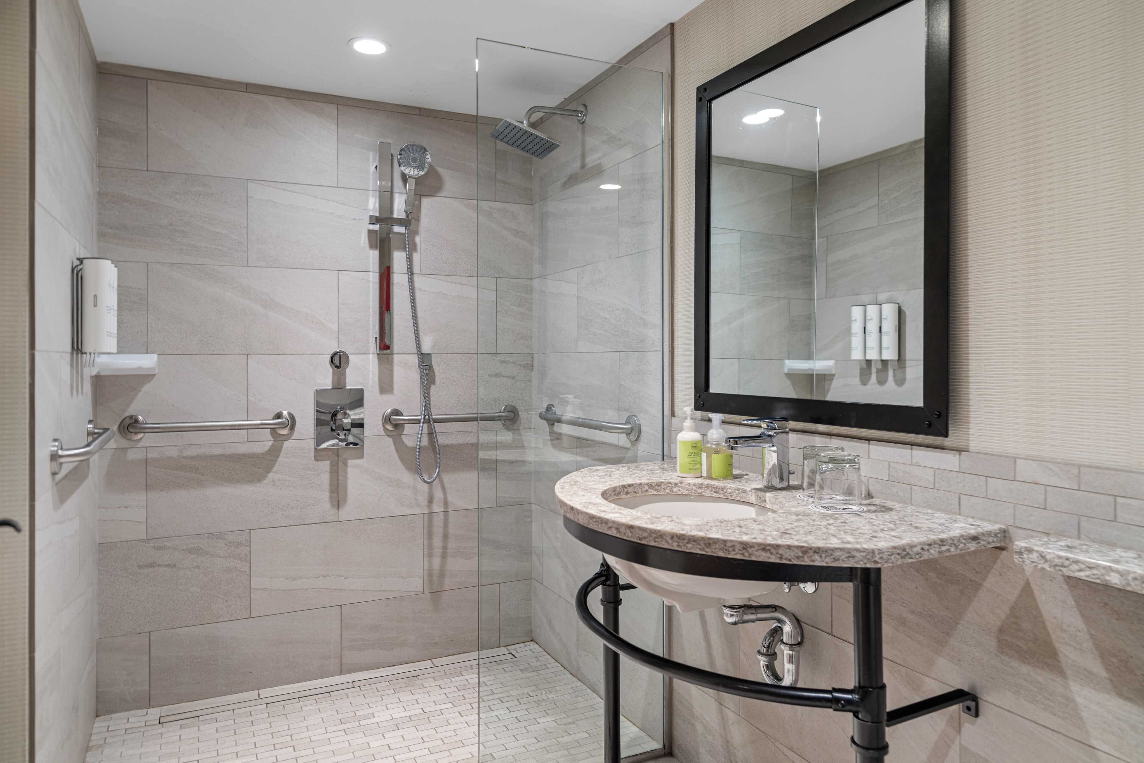 Un baño moderno con ducha de vidrio, tocador con lavamanos y un espejo grande.
