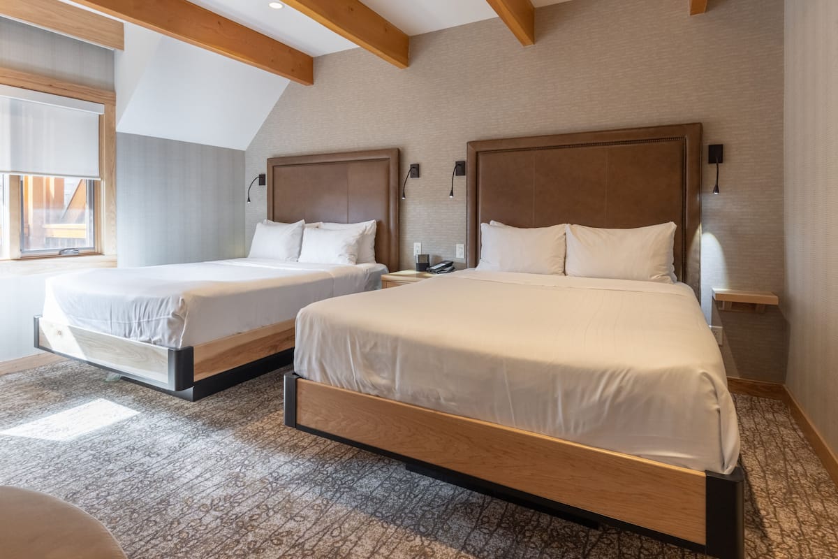 Une chambre d’hôtel avec deux lits, une grande fenêtre et un plafond en bois.