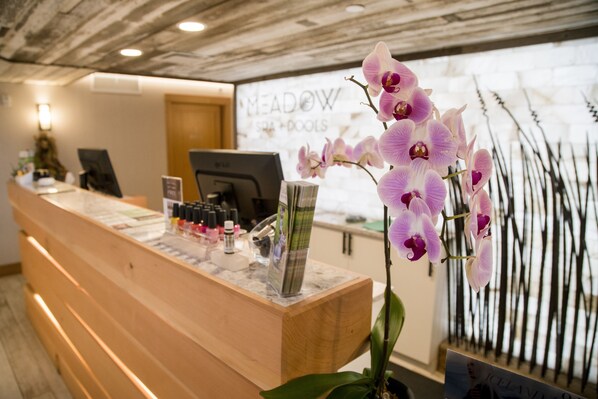 Een receptiebalie met een computer, een vaas met bloemen, en een bord met de tekst 'MEADOW SPA & DOOLS'.