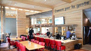 Een restaurant met houten tafels en rode stoelen, een bar en een bord met de tekst 'L'amore per la gente'.