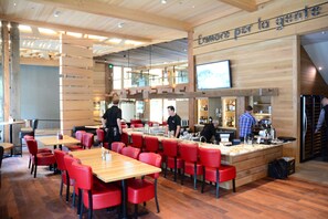 Un restaurant avec des tables en bois et des chaises rouges, un coin bar et une enseigne sur laquelle on peut lire : « L’amore per la gente ».