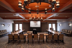 Une salle de conférence avec de longues tables et des chaises, un grand écran et un lustre.
