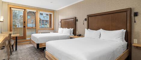 A hotel room with two beds, a desk, and a view of the outside.