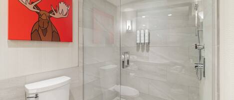 Un baño moderno con ducha envuelta en vidrio, inodoro y un cuadro de un alce rojo en la pared.