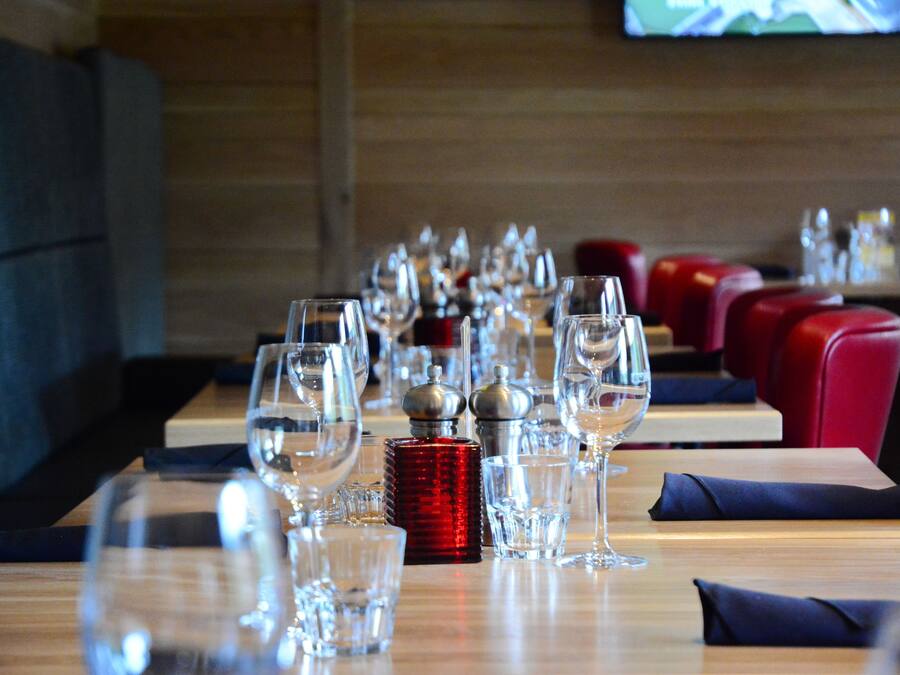 A restaurant with tables set for dining, featuring clear glassware and red salt and pepper shakers.