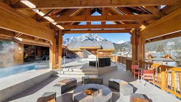 Une terrasse en bois avec un foyer, des sièges d’extérieur et une vue sur des montagnes enneigées.