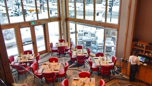 Een restaurant met grote ramen, rode stoelen en gedekte tafels.