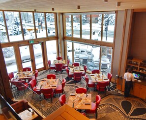 Un restaurant doté de grandes fenêtres, de chaises rouges et de tables dressées pour le service.