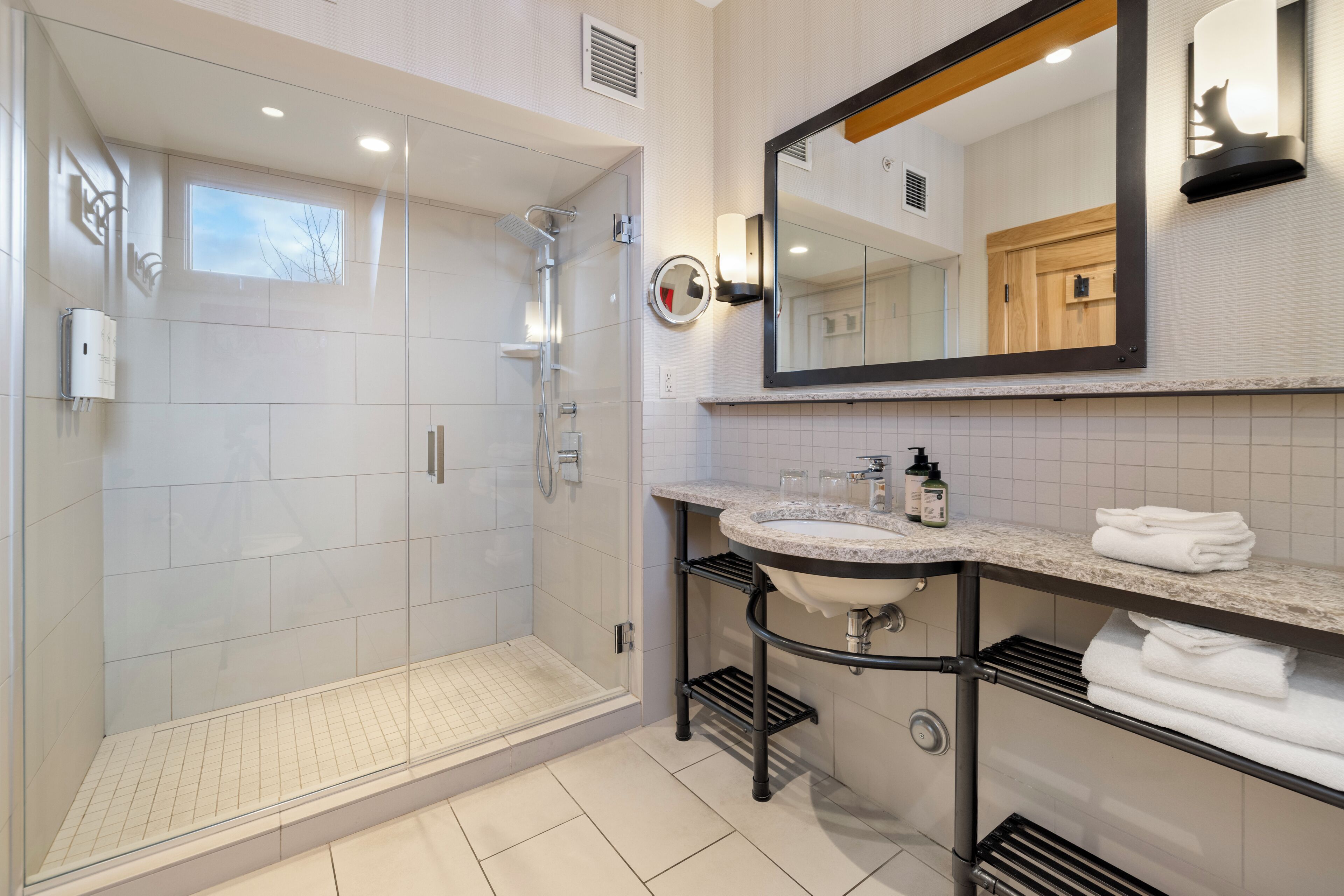 Un baño moderno con ducha envuelta en vidrio, tocador con lavabo y un espejo grande.