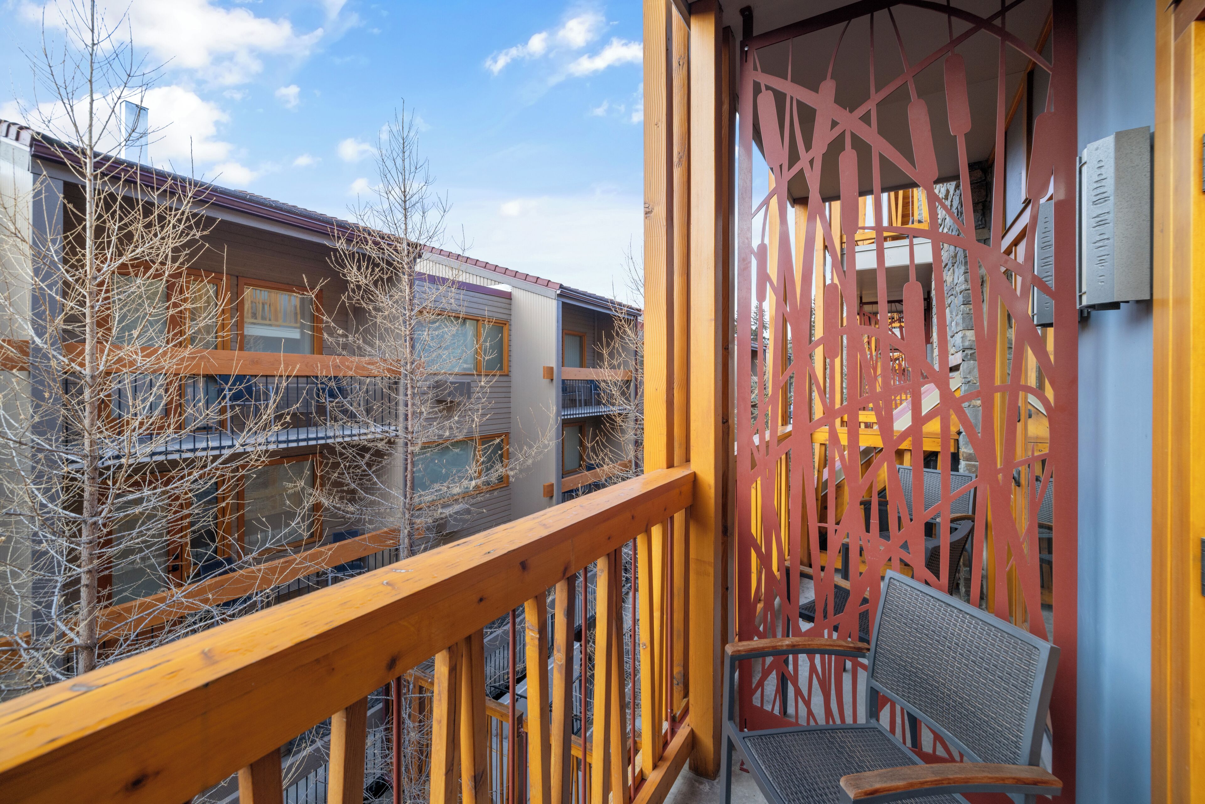 A balcony with a wooden railing, a chair, and a view of adjacent buildings.